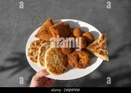 Authentic Sri Lankan different street food, short eats served in white plate in womans hand. Vegetable roti, Chinese rolls, coconut roti, cutlets, mut Stock Photo