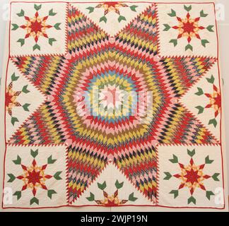 Star of Bethlehem quilt.  "Star of Bethlehem" pieced with diamond-shaped blocks of pink, green, yellow, blue, red and brown, stars are eight pointed, corner blocks of smaller stars in red and yellow with two green diamonds at each of its eight points, half of this corner star at center of each side; bound with red, joined with unbleached muslin; quilting outlines each block, with diagonal quilting, 1 1/2" apart on white areas, stitches crude Stock Photo