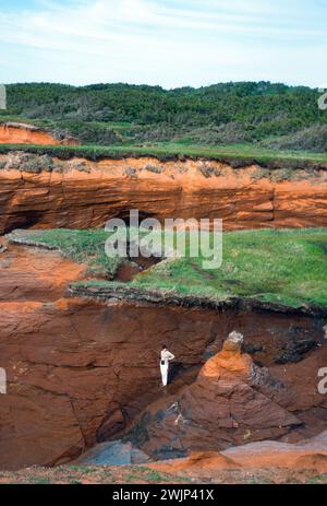 On the Magdalen Islands, Isles D' Madeleine, a tourist explores a sandstone fissure in a seawall cliff at Cap aux Meules Stock Photo