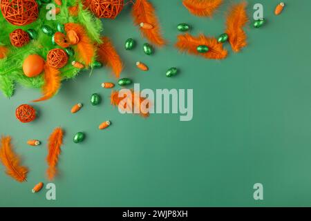 Decorative arrangement with feathers and chocolate eggs in green and orange on a green surface Stock Photo