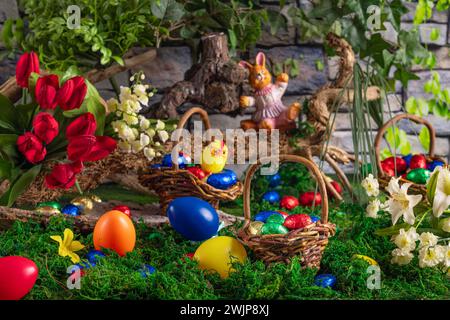 Easter basket with colourful eggs next to spring flowers and an Easter bunny on a moss-covered surface Stock Photo