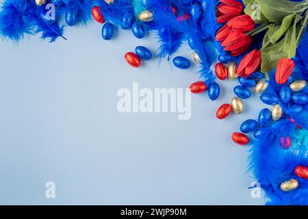 Colourful composition with blue feathers, red tulips and Easter eggs on a blue background Stock Photo