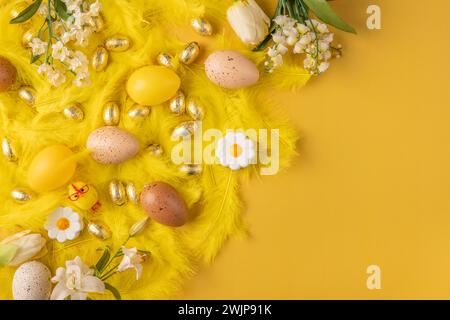 Festive Easter decorations with yellow feathers, yellow Easter eggs and spring flowers on a yellow background Stock Photo