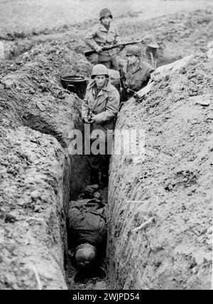 Ninth U.S. Army launches surprise Assault -- Infantrymen of the Ninth U.S. Army clear a captured slit trench where a dead Nazi soldiers lies face downward on Reich soil. Ninth Army forces, which were moved secretly across France, Belgium and Holland and placed on a front between Geilenkirchen and Eschweiler, Germany, captured five German towns in the first few hours of fighting after a new all-out offensive was launched November 16, 1944. by six allied armies closing in on the Reich. December 17, 1944. (Photo by Keystone Photo). Stock Photo