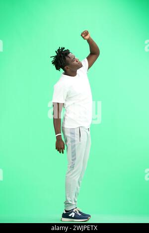 A man, full-length, on a green background, raised his hand up Stock Photo