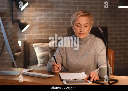 Mature female programmer working in office at night Stock Photo