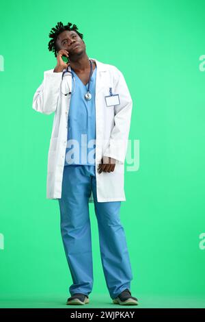 The doctor, in full height, on a green background, talking on the phone. Stock Photo