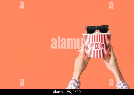 Female hands with bucket of popcorn and 3D glasses on orange background Stock Photo