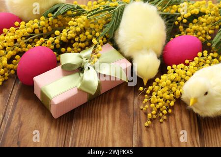 Beautiful Easter composition with painted pink eggs, chickens, mimosa and gift box on wooden table Stock Photo