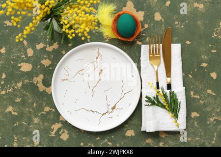 Stylish table setting for Easter celebration  with Easter egg and mimosa on green background Stock Photo