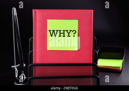 WHY Text on a yellow sticker on a red vertical notepad on a black background next to a pen and money Stock Photo