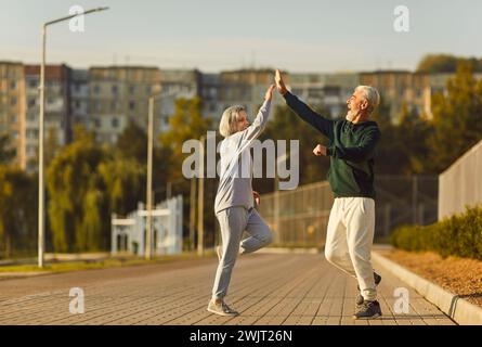 Active senior happy pair running high five, sporty physically energetic older man, woman outdoor Stock Photo