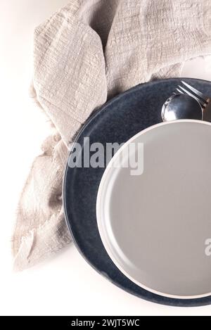 table setting with two empty ceramic gray plate with cutlery and and a napkin on white table. Neutral colors. Stock Photo