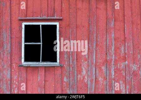 Red wall with weathered boards and cracked paint. Broken window frame without glass. Stock Photo