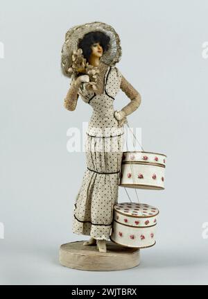 Lafitte-Désirat (active between 1902 and 1904). Fashion figurine: Midinette or elegant wearing two hat boxes. Doll, wax, mohair, leather, paper, metal, clothing, white silk taffetas printed with black peas, black silk shop, small fabric flowers (cream taffeta cream, metal, green paper), horsehair (?) And ribbon and ribbon Braided crushed silk, white cotton mechanical lace, cardboard, printed paper, golden paper, silk tulle (known as tulle illusion) ecru. On the beige silk taffeta base with a large, fluted frame, bottom of the base covered with pink glued canvas. 1906-1907. Galliera, fashion mu Stock Photo