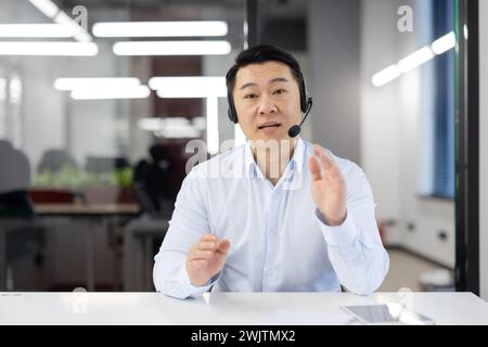 Asian businessman with headset in modern office providing customer support or leading a team meeting, displaying engagement. Stock Photo