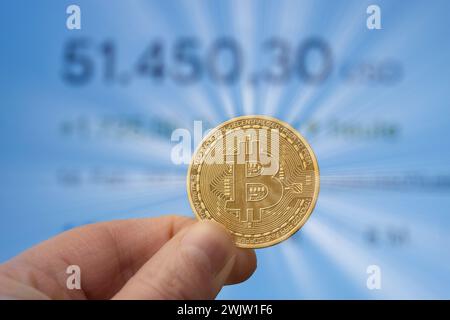 Bitcoin coin between fingers in front of a market price of over 50,000 USD Stock Photo