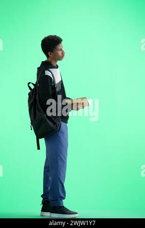 A man, full-length, on a green background, with a backpack, writes Stock Photo