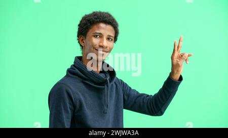 A man, close-up, on a green background, shows a victory sign Stock Photo