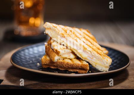 Sliced Cut Toast sandwich with molten Gouda cheese and turkey ham on a wooden background with cherry tomato on a black plate. Served with ice tea. Stock Photo