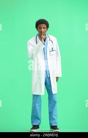 The doctor, in full height, on a green background, shows a sign of silence Stock Photo