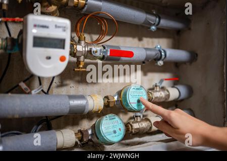 A woman's finger points to the water meters of cold and hot water consumption in real apartments in Europe Stock Photo