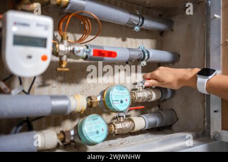 A woman's hand closes a hot water pipe to save money, water meters of cold and hot water, water consumption in real apartments, Europe Stock Photo