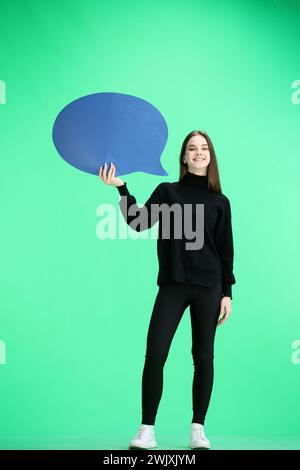 A woman, full-length, on a green background, shows a blue comment sign Stock Photo
