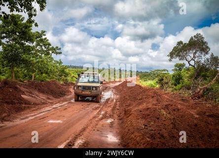 A 4-wheel drive vehicle drives down a wet and muddy red earth road near Msanga in rural Tanzania. Stock Photo