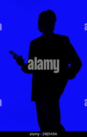 Silhouette an elegant businessman using a modern smartphone in a jacket standing on a blue glowing background, a futuristic concept Stock Photo