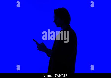 Silhouette an elegant businessman using a modern smartphone in a jacket standing on a blue glowing background, a futuristic concept Stock Photo