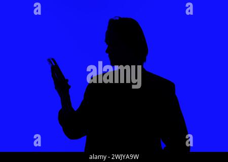 Silhouette an elegant businessman using a modern smartphone in a jacket standing on a blue glowing background, a futuristic concept Stock Photo