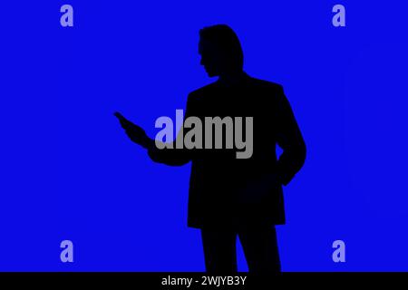 Silhouette an elegant businessman using a modern smartphone in a jacket standing on a blue glowing background, a futuristic concept Stock Photo