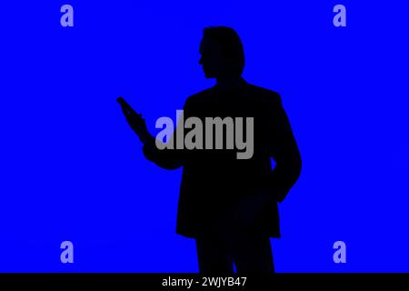 Silhouette an elegant businessman using a modern smartphone in a jacket standing on a blue glowing background, a futuristic concept Stock Photo