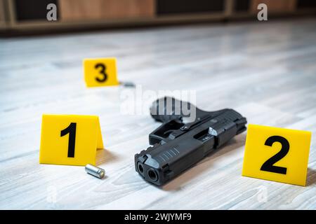 Augsburg, Bavaria, Germany - February 16, 2024: Symbolic image crime scene after a shooting spree staged scene. Pistol with shell casings scattered on the ground with police evidence markings *** Symbolbild Tatort nach einer Schießerrei gestellte Szene. Pistole mit Patronenhüsel auf dem Boden verteilt mit Beweismittel Markierungen der Polzei Stock Photo