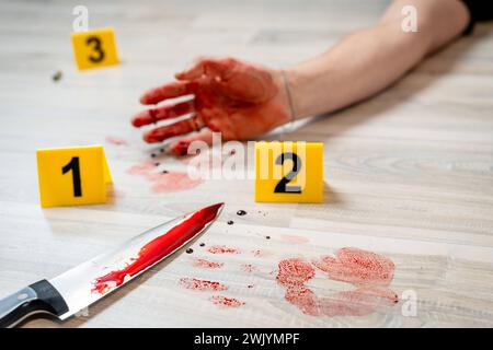 Augsburg, Bavaria, Germany - February 16, 2024: Symbolic image crime scene of a murder case staged scene. Man smeared with blood lying on the ground with police evidence markings *** Symbolbild Tatort eines Mordfalls gestellte Szene. Mit Blut verschmierter Mann liegt auf dem Boden mit Beweismittel Markierungen der Polizei Stock Photo