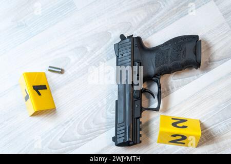 Augsburg, Bavaria, Germany - February 16, 2024: Symbolic image crime scene after a shooting spree staged scene. Pistol with shell casings scattered on the ground with police evidence markings *** Symbolbild Tatort nach einer Schießerrei gestellte Szene. Pistole mit Patronenhüsel auf dem Boden verteilt mit Beweismittel Markierungen der Polzei Stock Photo