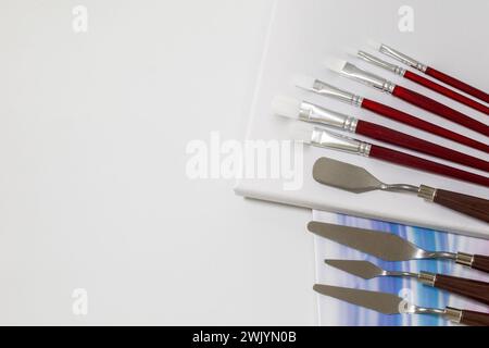 Art painting supplies  - brushes, painting knives, canvas, painted paper - located in the right part of the photo and isolated on the white background Stock Photo