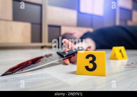 Augsburg, Bavaria, Germany - February 16, 2024: Symbolic image crime scene of a murder case staged scene. Man smeared with blood lying on the ground with police evidence markings *** Symbolbild Tatort eines Mordfalls gestellte Szene. Mit Blut verschmierter Mann liegt auf dem Boden mit Beweismittel Markierungen der Polizei Stock Photo