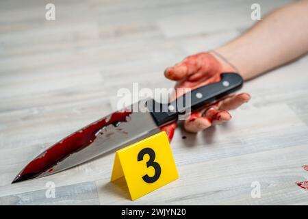 Augsburg, Bavaria, Germany - February 16, 2024: Symbolic image crime scene of a murder case staged scene. A man lies dead on the floor in an apartment.Markings from police evidence and a murder weapon smeared with blood, a knife Markings from police evidence and a murder weapon smeared with blood, a knife *** Symbolbild Tatort eines Mordfalls gestellte Szene. Ein Mann liegt tot auf dem Boden in einer Wohnung. Markierungen von Beweisstücken der Polizei und mit Blut verschmierte Tatwaffe, ein Messer Stock Photo