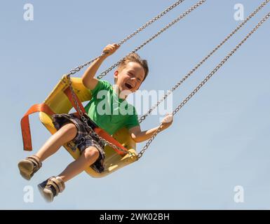 Joy thrill and fun are the emotions of a young boy swinging on a ride at the local carnival with blue sky. Stock Photo