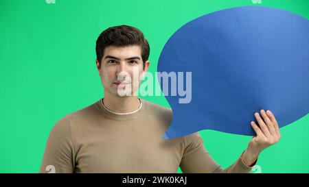 A man, close-up, on a green background, shows a blue comment sign Stock Photo