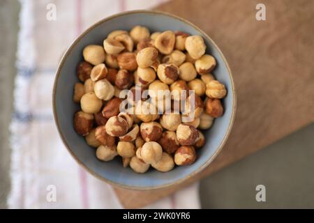 A Close-up of a bowl of hazelnuts on wood board with a napkin in the background Stock Photo