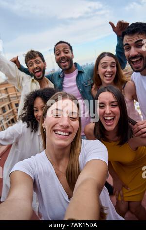 Young pretty woman taking group selfie with joyful friends on rooftop. Cheerful people excited photo Stock Photo