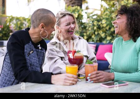 Cheerful gathering mature multi-ethnic female friends laughing outdoor. Smiling group three women. Stock Photo