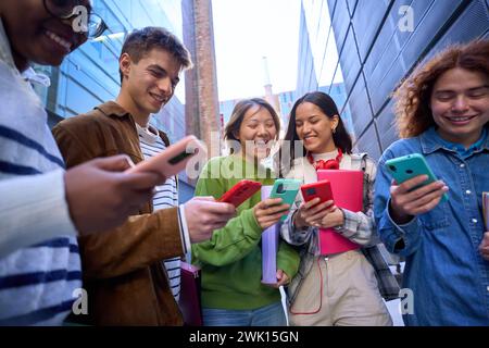 Group young people in circle using phones together outdoor. Cheerful friends meeting having fun. Stock Photo