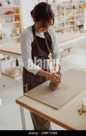 Pretty woman preparing clay to create a mug on a wooden table in pottery studio Stock Photo