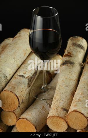 Red wine in wineglass on wooden logs against black background Stock Photo
