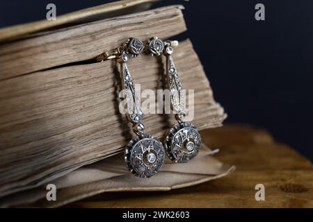 A 19th century earrings resting on a book from ancient Mesopotamia and on a wooden table Stock Photo
