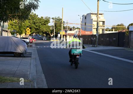 Rear view of a Fantuan delivery rider, on a bike, as they travel down a quiet and shady suburban Melbourne street Stock Photo